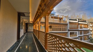 A corridor with a wooden railing, leading to a building with traditional architecture. - The Kaal (Leh)