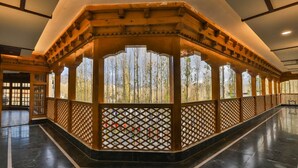 A corridor with a wooden lattice railing, a tiled floor, and a view of trees through the railing. - The Kaal (Leh)