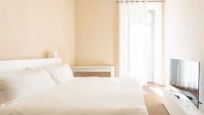A hotel room with a large bed, a TV on a white cabinet, a desk, and a window with curtains. - Suite Cavour by icasamia.it (Varese)