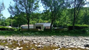 Une propriété située au bord de la rivière, avec un bâtiment en pierre, entourée d’une végétation luxuriante et d’arbres.