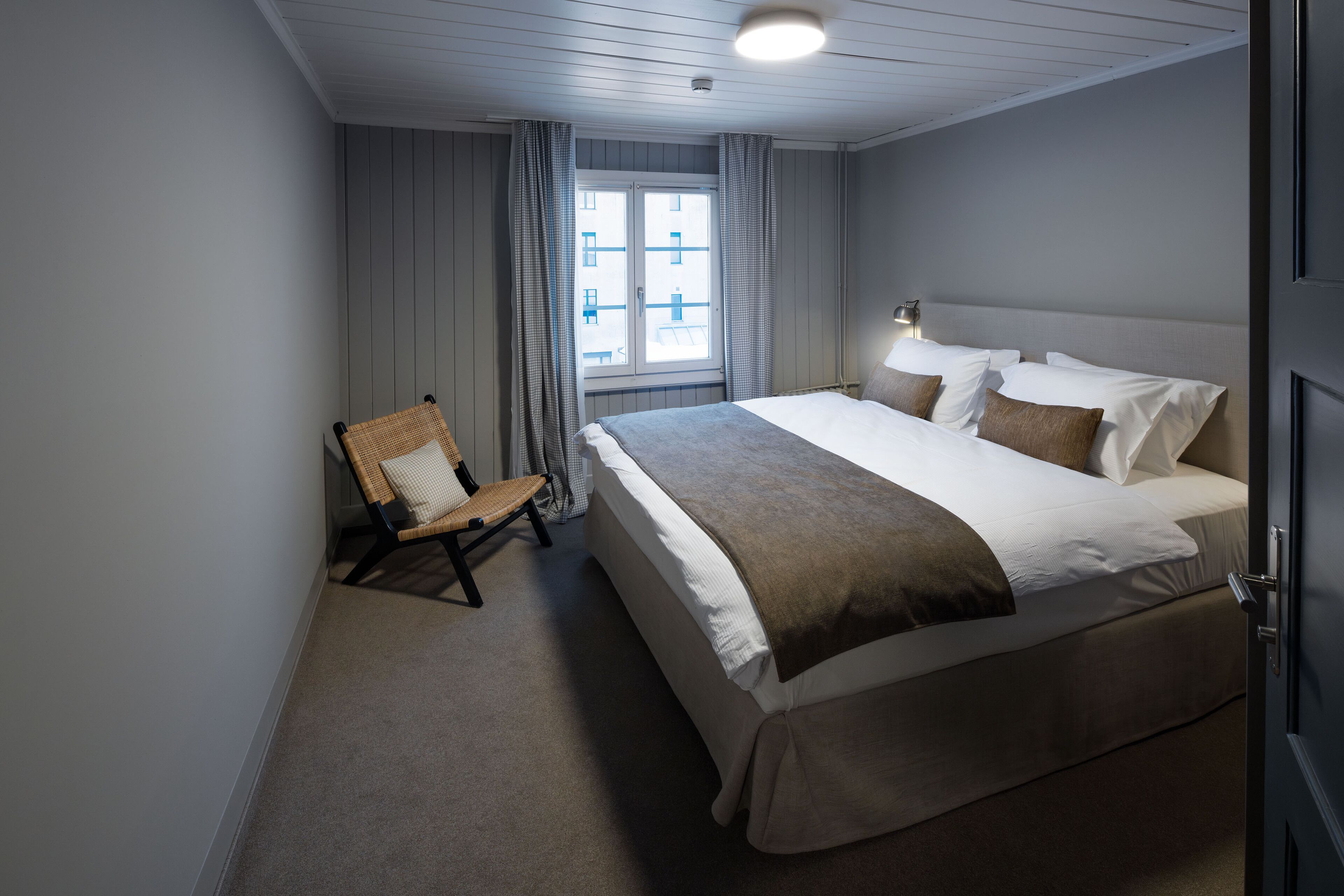 A bedroom with a large bed, a chair, and a window with curtains.