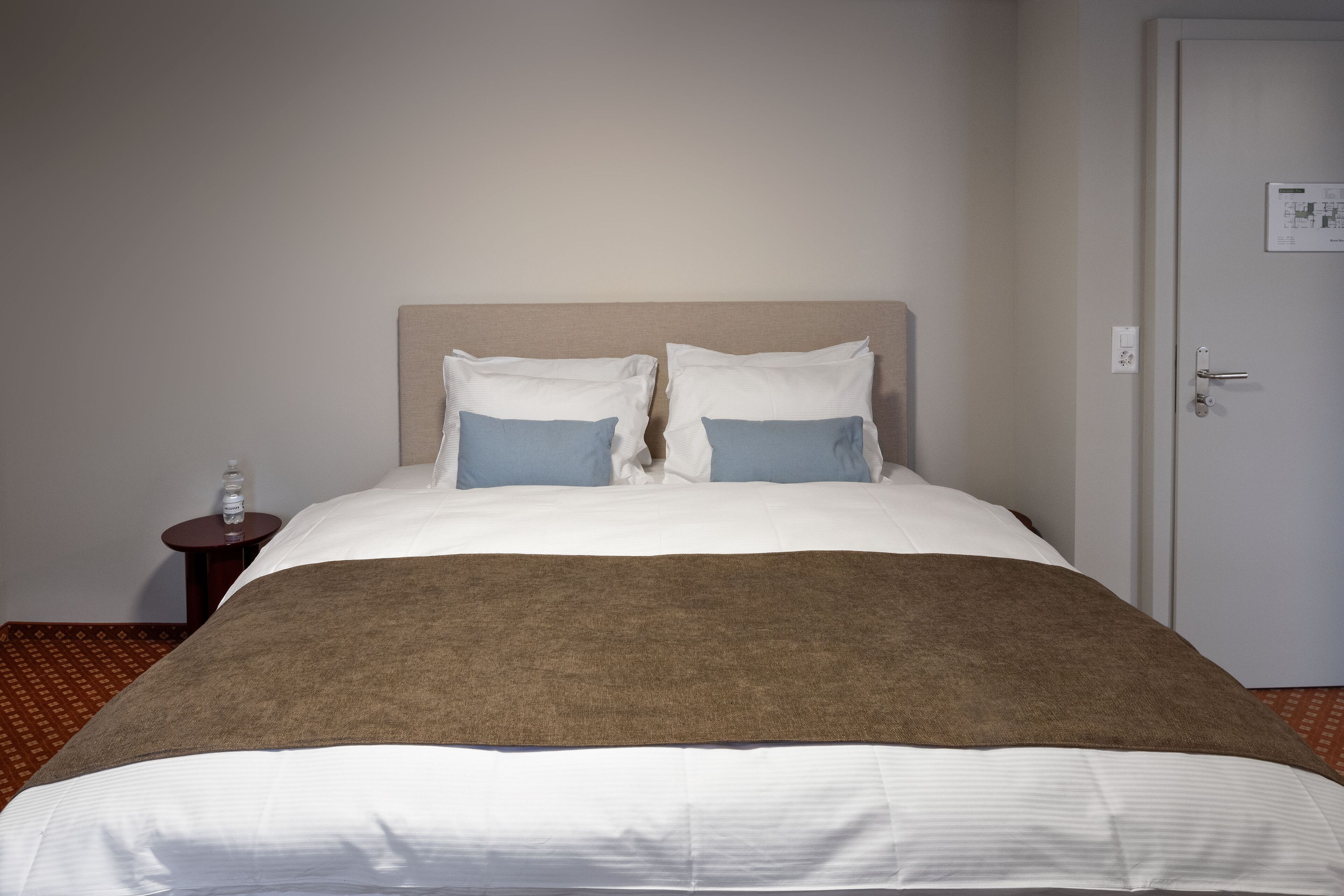 Ein ordentlich bezogenes Bett mit einer braunen Decke, weißen Laken und zwei blauen Kissen.