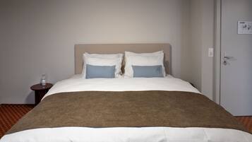 A neatly made bed with a brown blanket, white sheets, and two blue pillows.