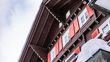 Ein mehrstöckiges Gebäude mit roten Fensterläden und Schnee auf dem Dach.