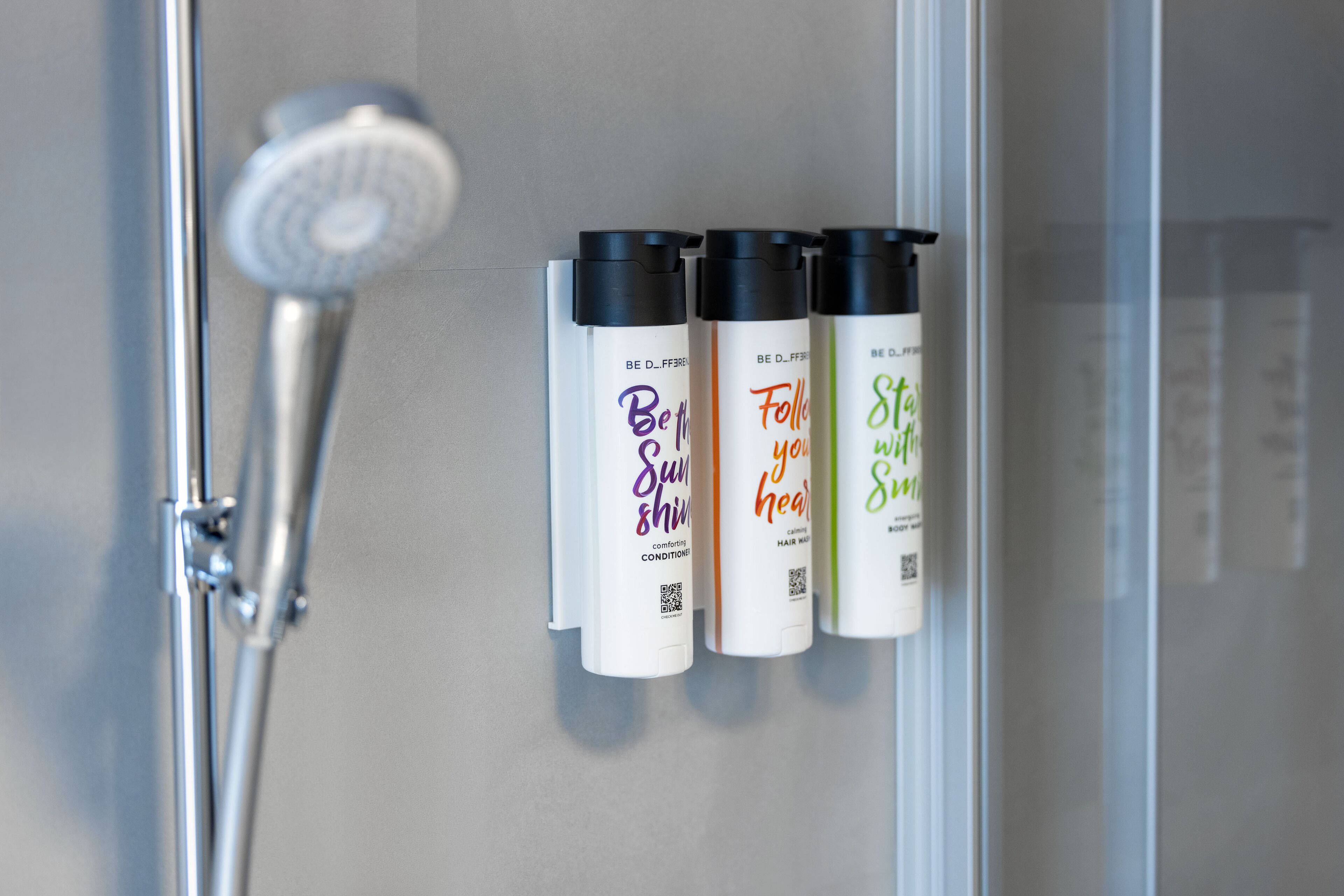 Un baño con ducha y tres botellas de productos para el cabello en la pared.