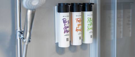 Un baño con ducha y tres botellas de productos para el cabello en la pared.