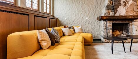 A yellow sofa with multiple pillows, a stone fireplace, and a wooden ceiling.
