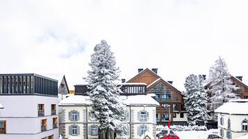Een besneeuwde woonwijk met moderne gebouwen, waaronder een meerlaags gebouw met balkons en een chalet in traditionele stijl met een houten gevel.