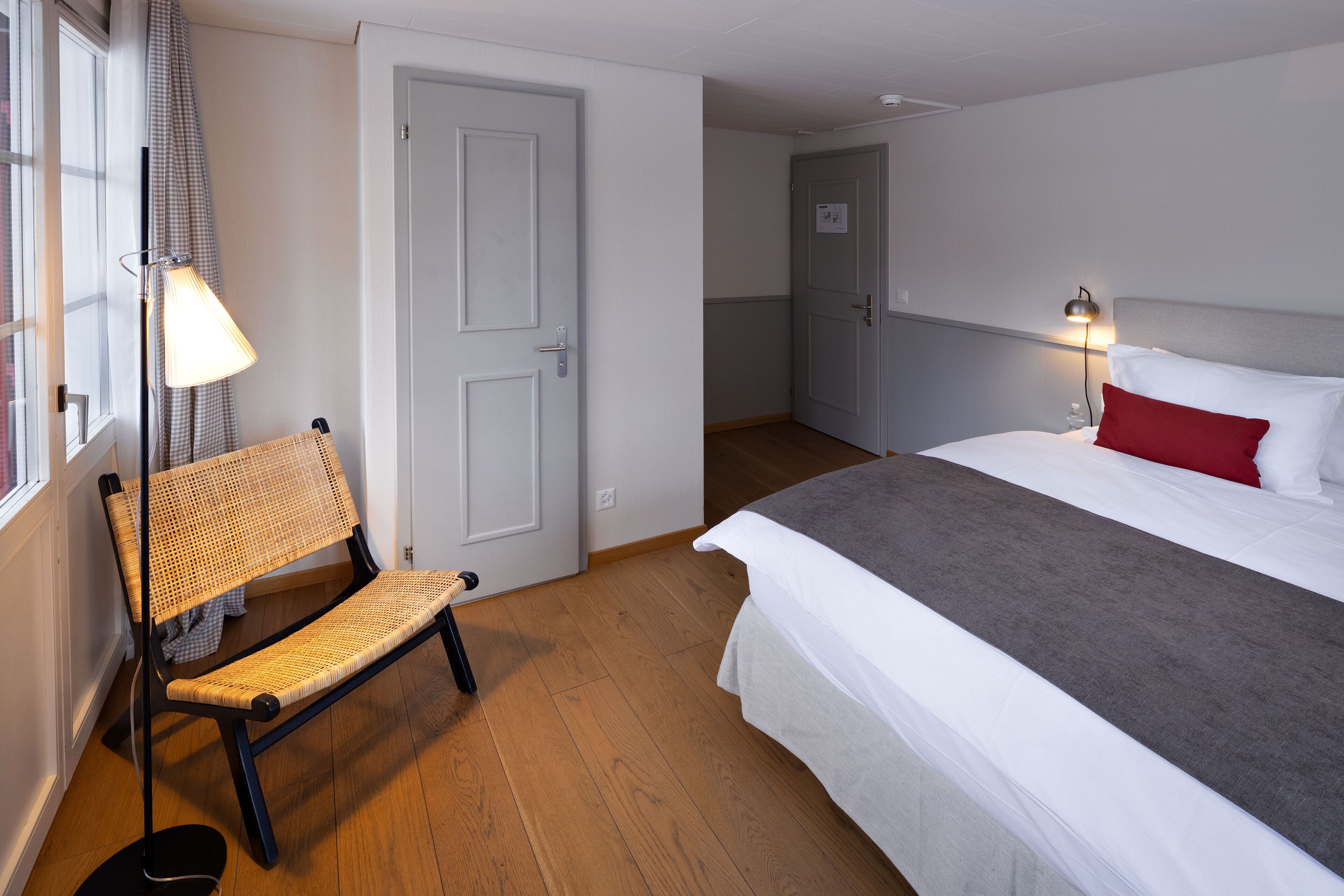 Een hotelkamer met een bed, een bankje, een lamp en een deur.