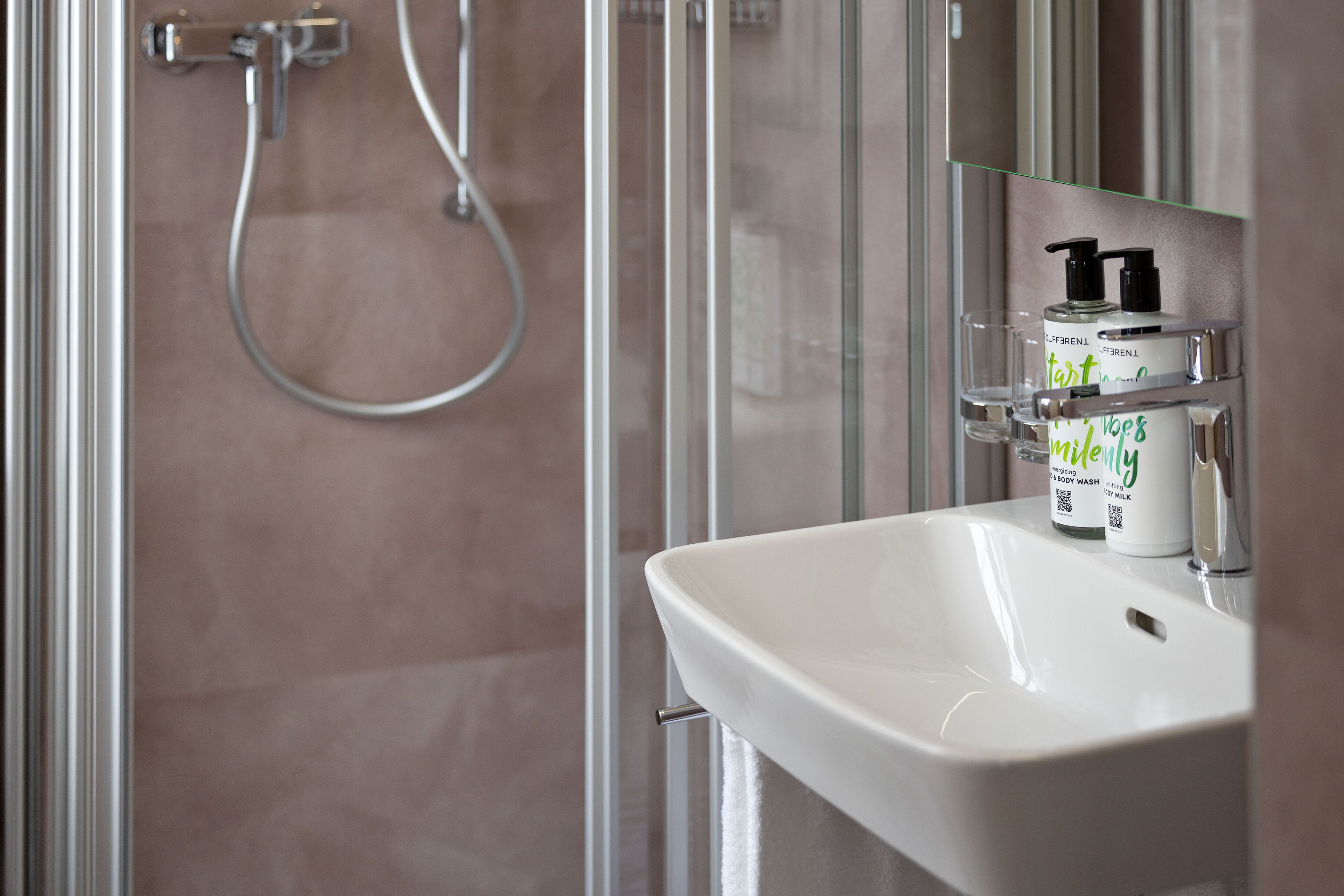 Un baño con lavamanos blanco, un espejo y zona de ducha.