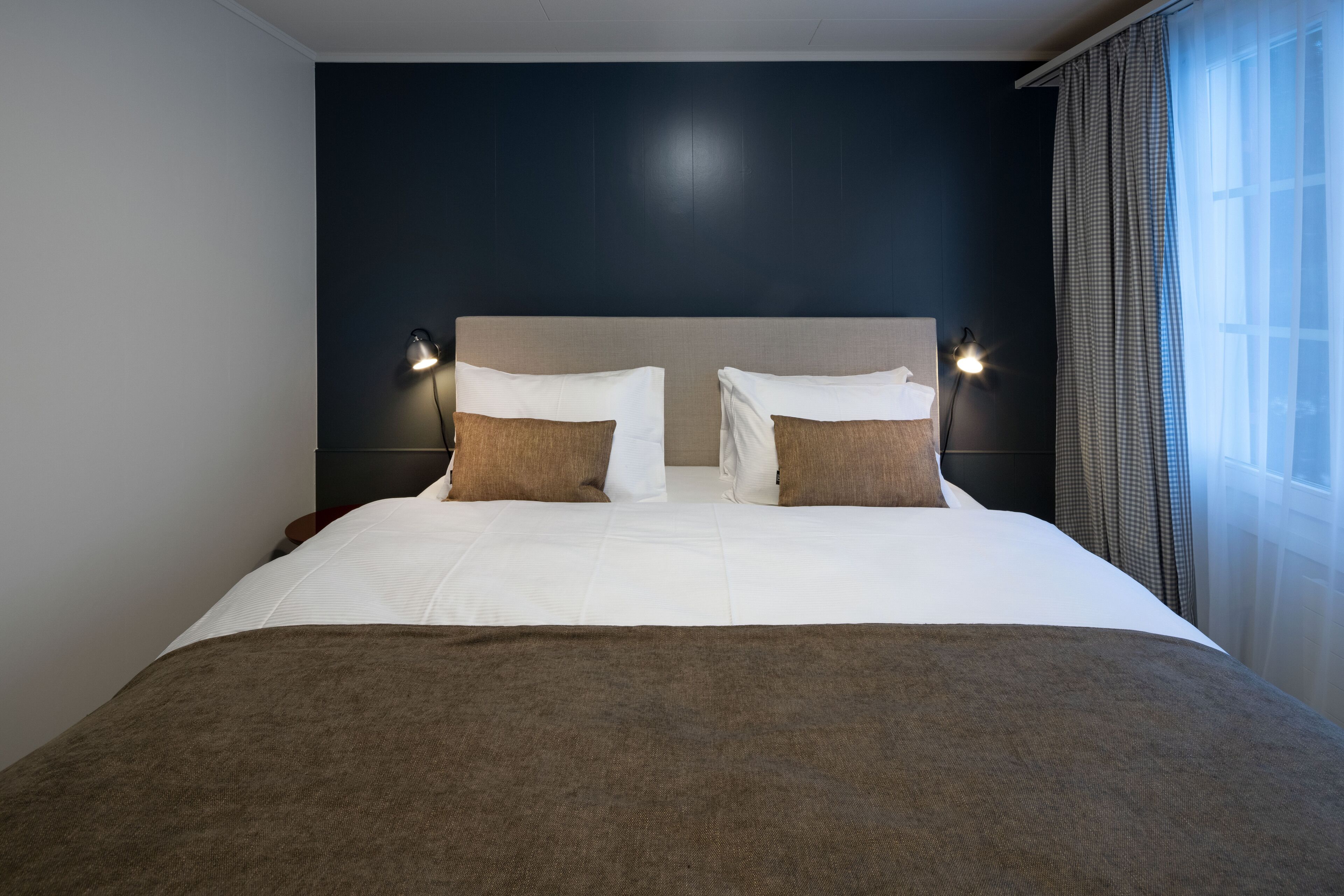 A large bed with a dark headboard, two bedside lamps, and a window with curtains.