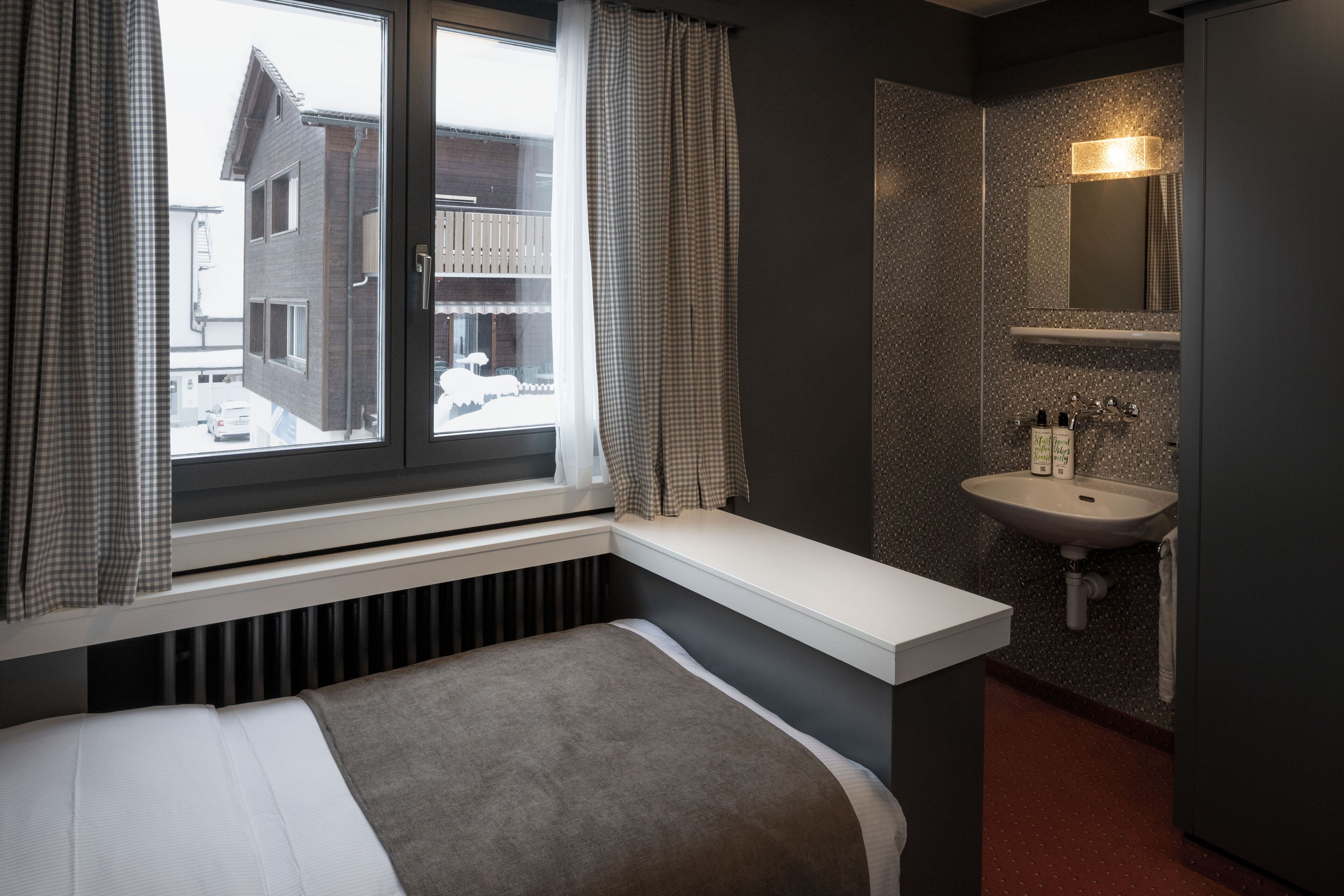 A hotel room with a bed, a window with curtains, a sink, and a mirror.