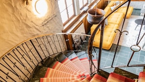 Una escalera en espiral con un suelo a rayas rojas y blancas, barandilla de madera y pasamanos de metal.
