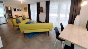 Un salon moderne avec un canapé jaune, une table à manger et une cuisine en arrière-plan.