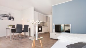 Une chambre d’hôtel moderne équipée d’un lit, d’une télévision, d’un coin repas avec des chaises et une table, et d’une cuisine en arrière-plan.