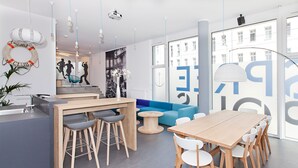 Un intérieur moderne avec une table à manger en bois, des chaises blanches, un canapé bleu et un coin cuisine équipé d’un évier et de tabourets de bar.