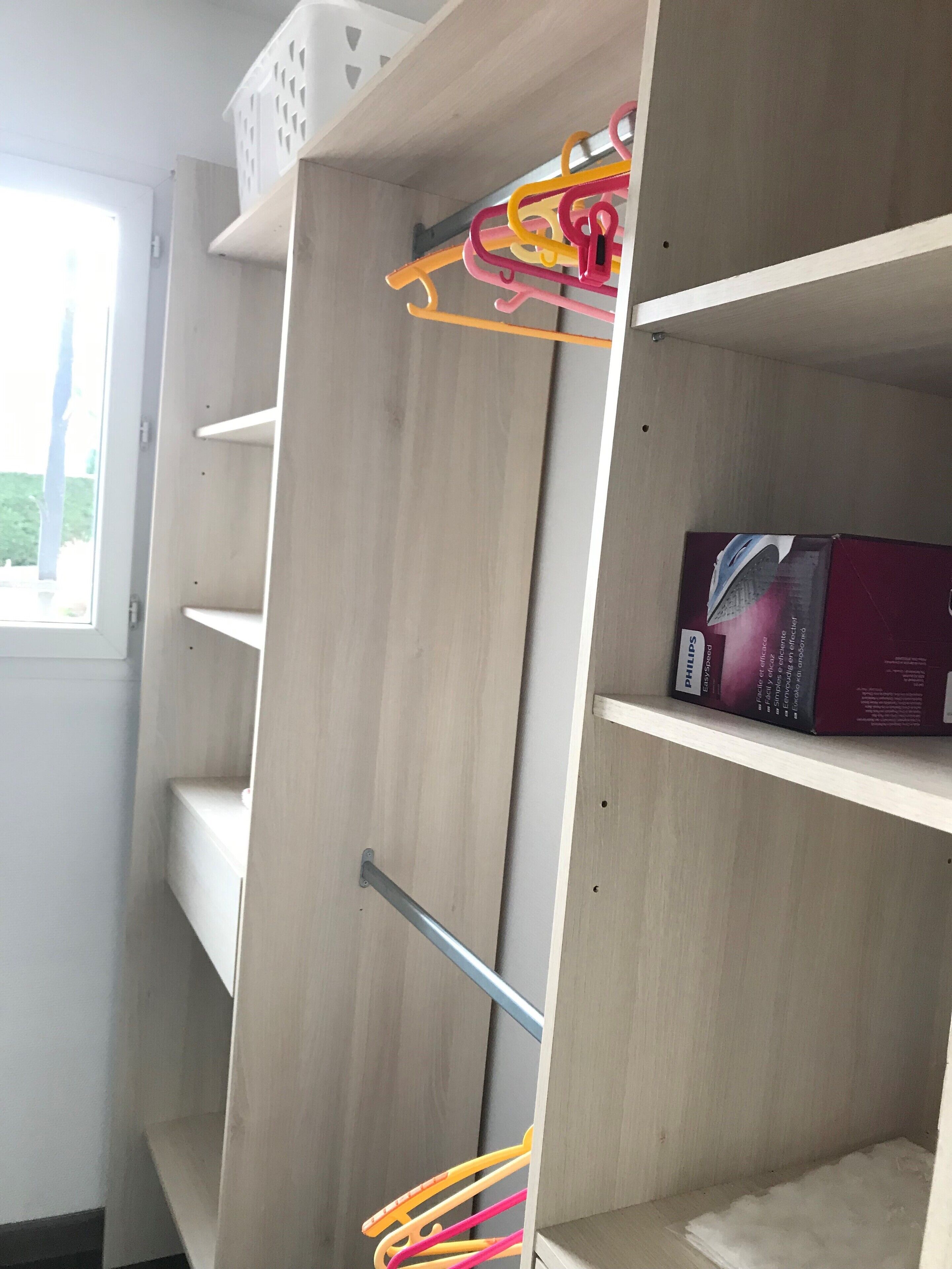 Ein Schrank mit Holzböden, einer Kleiderstange und einer Philips SpeedChef Mikrowellenverpackung auf der obersten Ablagefläche.