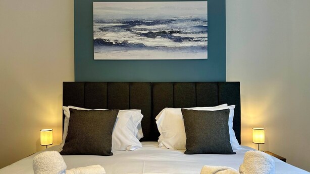 A hotel room with a large bed, two bedside lamps, and a painting of a seascape on the wall. - 2 Bedroom House in Central Winchester (Winchester)