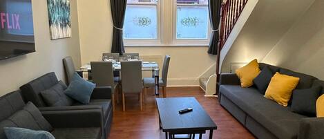 Una sala de estar moderna con un conjunto de sofá, una mesa de comedor y un televisor montado en la pared.