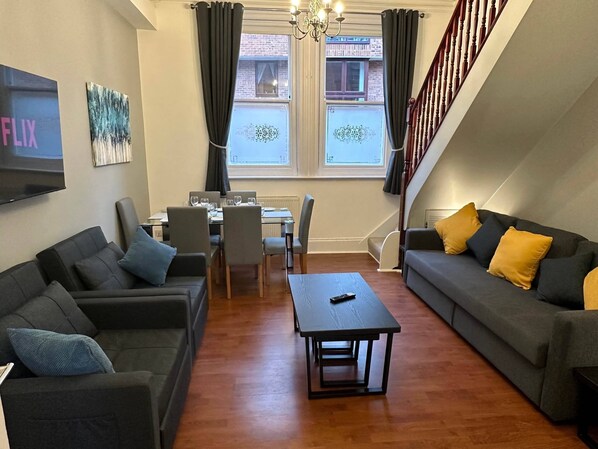 A modern living room with a sofa set, a dining table, and a TV mounted on the wall. - 2 Bedroom House in Central Winchester (Winchester)