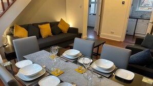 A dining area with a glass table set for six, surrounded by grey chairs. A dark grey sofa with yellow cushions is in the background. - 2 Bedroom House in Central Winchester (Winchester)
