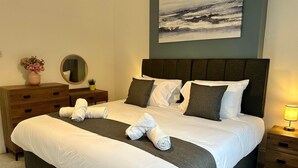 A neatly made bed with white linens and rolled towels, a bedside table with a lamp, a dresser with a mirror, and a painting on the wall. - 2 Bedroom House in Central Winchester (Winchester)