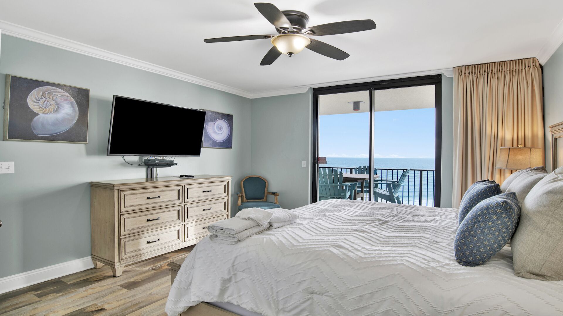 Een slaapkamer met een bed, een televisie, een dressoir, een stoel en een balkon met uitzicht op zee.