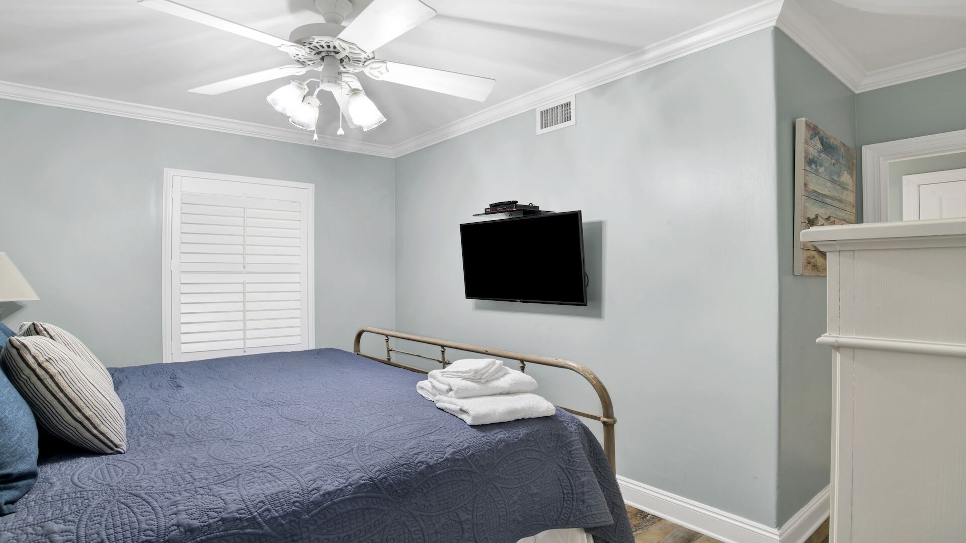 A bedroom with a bed, a ceiling fan, a mounted TV, and a white door.