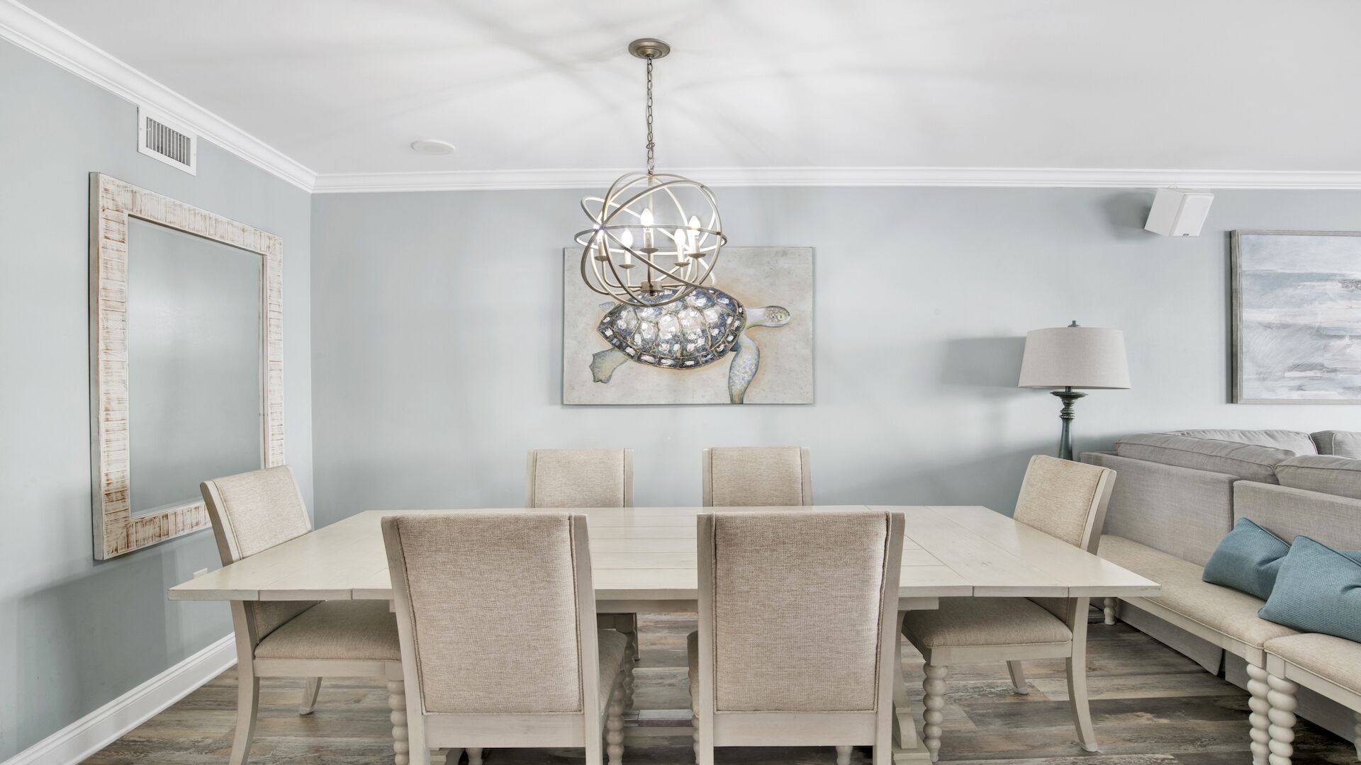 Un comedor con una mesa rectangular, cuatro sillas, una lámpara de araña y un sofá al fondo.