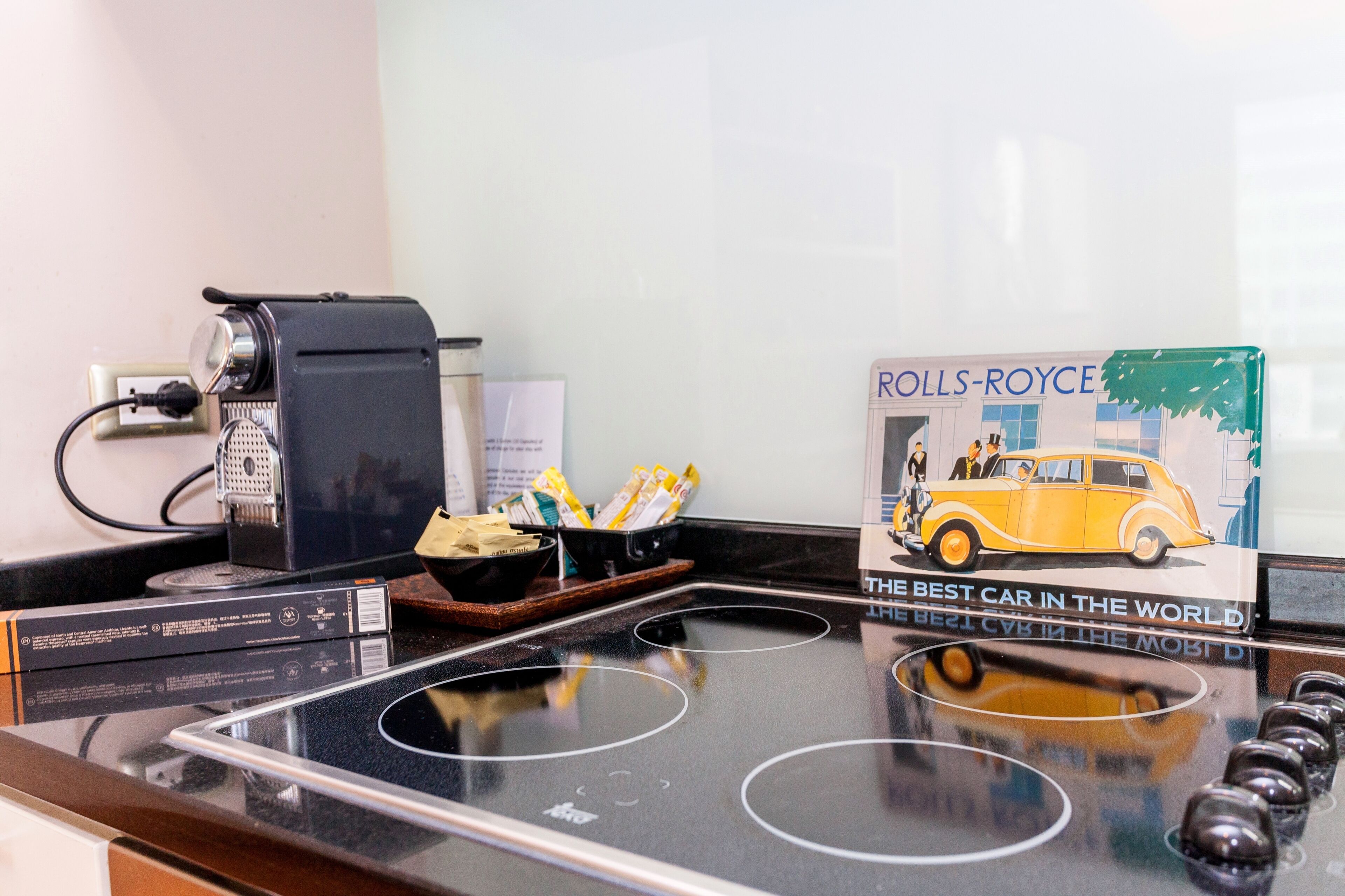 A kitchen counter with a coffee machine, a bowl of snacks, and a Rolls-Royce advertisement.