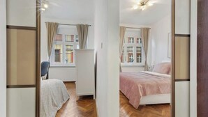 Ein Schlafzimmer mit Bett, Sessel, Fenster mit Vorhängen und Heizkörper.