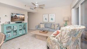 A living room with a teal cabinet, a light blue sofa, a patterned armchair, a coffee table, and a ceiling fan. - A view of Gulf of Mexico, plus access to all the resort amenities! A3214C (Placida)