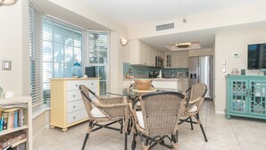 A modern kitchen with white cabinets, a stainless steel refrigerator, and a dining area with wicker chairs and a glass table. - A view of Gulf of Mexico, plus access to all the resort amenities! A3214C (Placida)