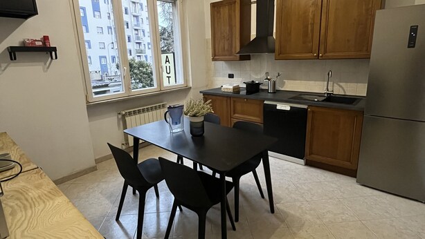 A modern kitchen with wooden cabinets, a stainless steel refrigerator, and a dining table with chairs. - Rome 23, apartment in Rozzano (Rozzano)