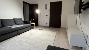 A modern living room with a dark-colored sofa, a white coffee table, a floor lamp, and a TV mounted on the wall. - Rome 23, apartment in Rozzano (Rozzano)