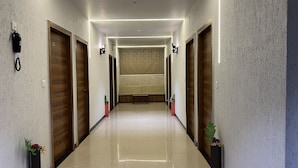 A hallway with wooden doors, a bench, and potted plants. - Hotel Near Me (Rajkot)