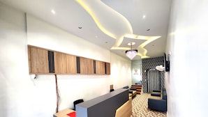 A hotel reception area with a reception desk labeled "RECEPTION," a chandelier, and a seating area with a black and white patterned floor. - Hotel Near Me (Rajkot)