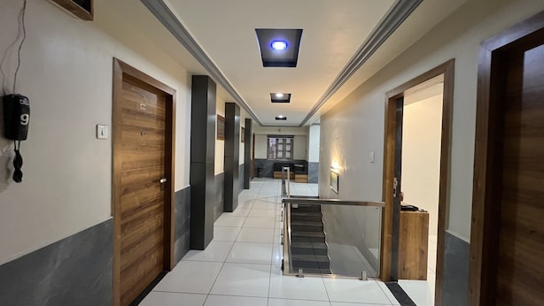 A hotel hallway with wooden doors, a staircase, and a ceiling light. - Hotel Near Me (Rajkot)