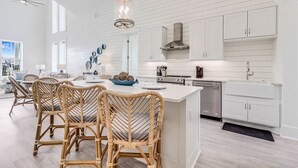 A modern kitchen with white cabinetry, a central island, wicker chairs, and a ceiling fan.