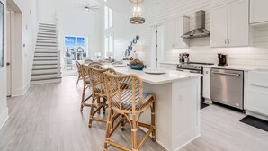 A modern kitchen with white cabinetry, a central island with bar stools, and a stainless steel dishwasher.