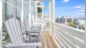 A wooden deck with Adirondack chairs, a white railing, and a view of houses in the background.
