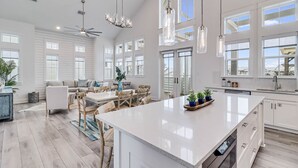 Cocina amplia con una isla grande, armarios blancos e iluminación colgante.