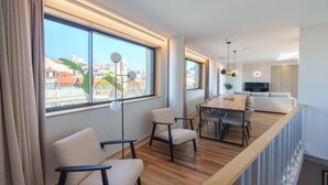 A modern living room with a wooden dining table, two sofas, and a large window with a view of buildings.