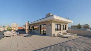 A rooftop terrace with a modern lounge area, including seating and umbrellas, overlooking a cityscape.