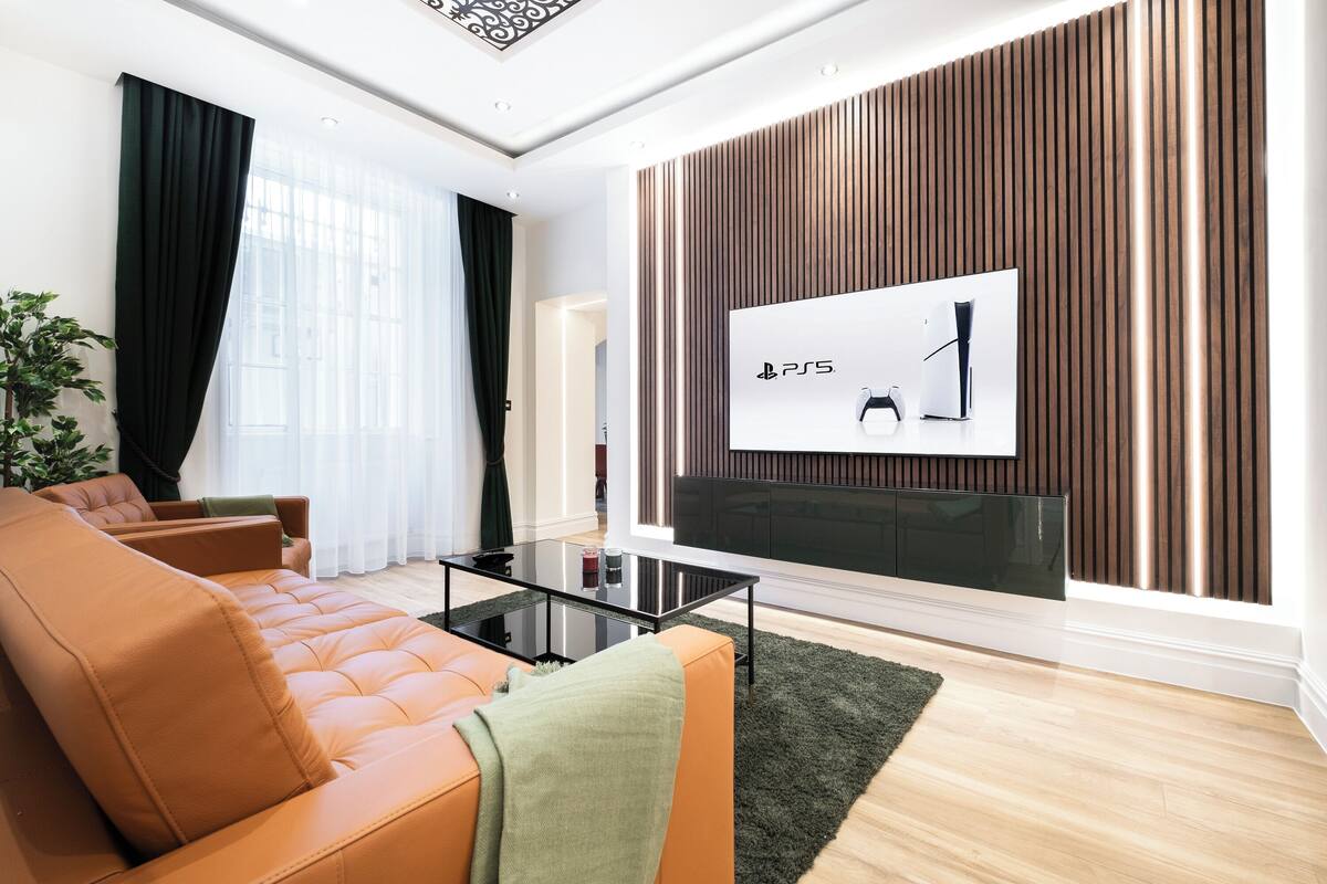 A modern living room with a leather sofa, a glass coffee table, and a flat-screen TV mounted on a wooden wall.