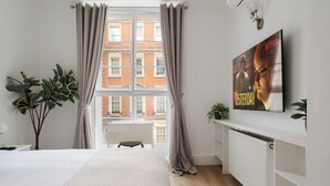 Hotellihuone, jossa on suuri ikkuna, sänky, patteri ja juliste seinällä.