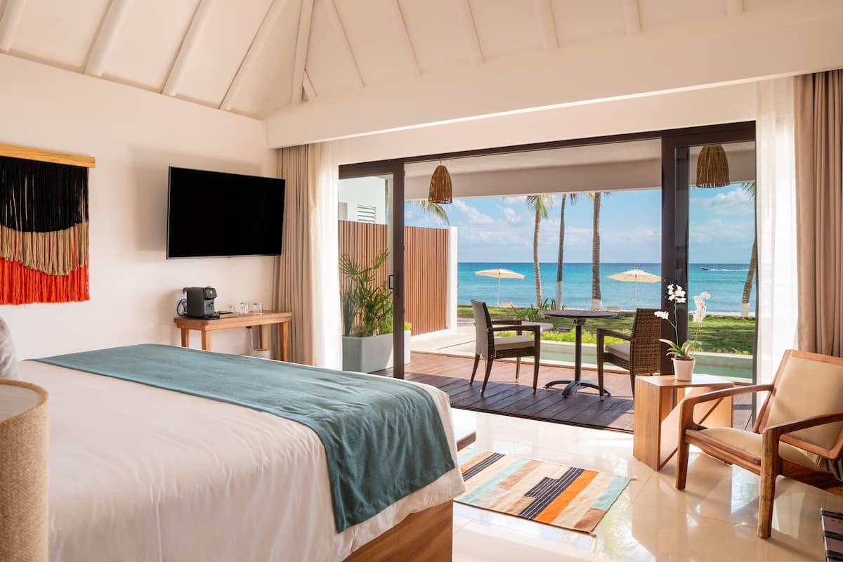 A bedroom with a bed, a TV, a coffee maker, and a view of the ocean through a sliding door.