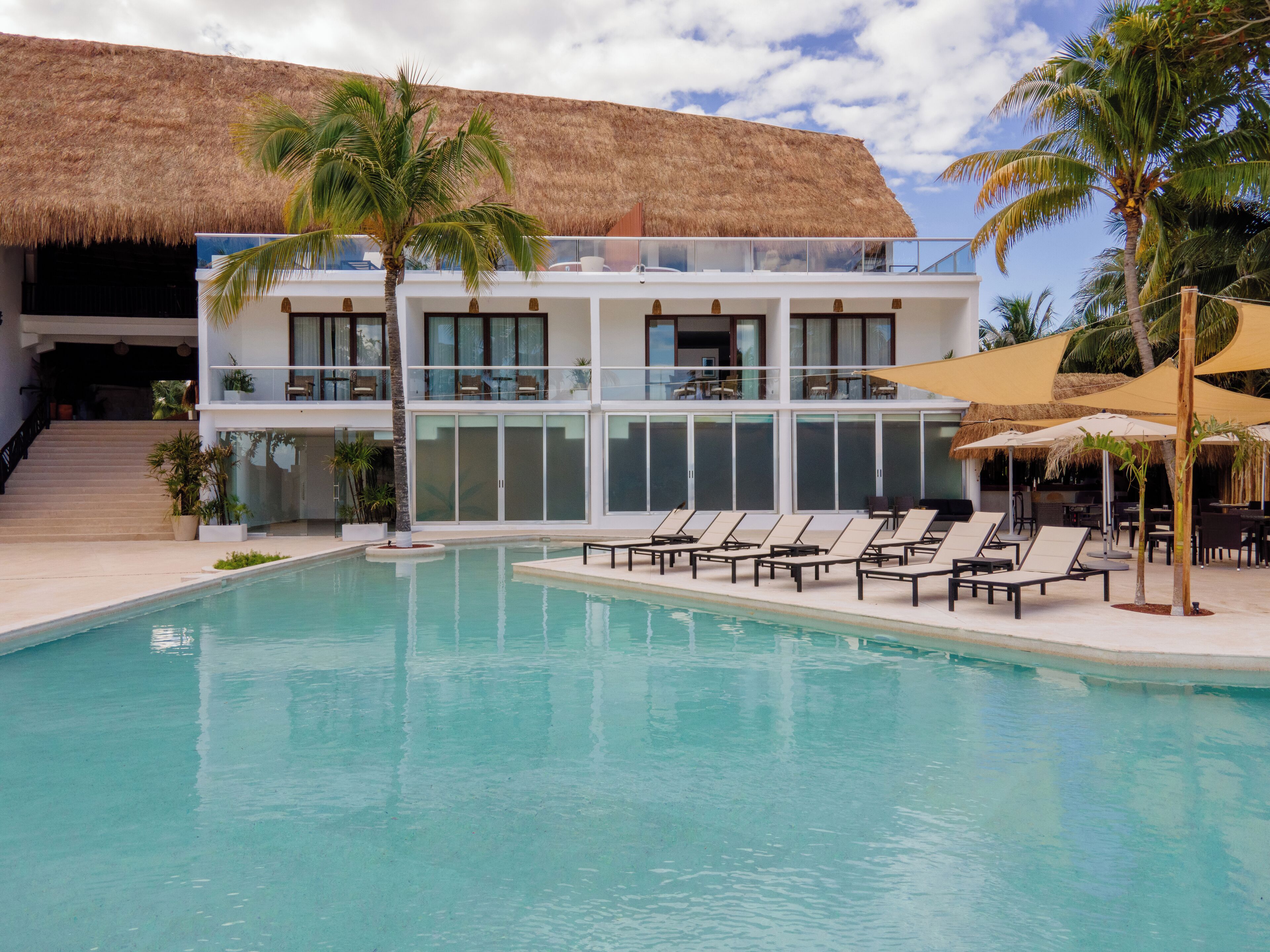 A resort with a swimming pool, lounge chairs, and a building with a thatched roof.