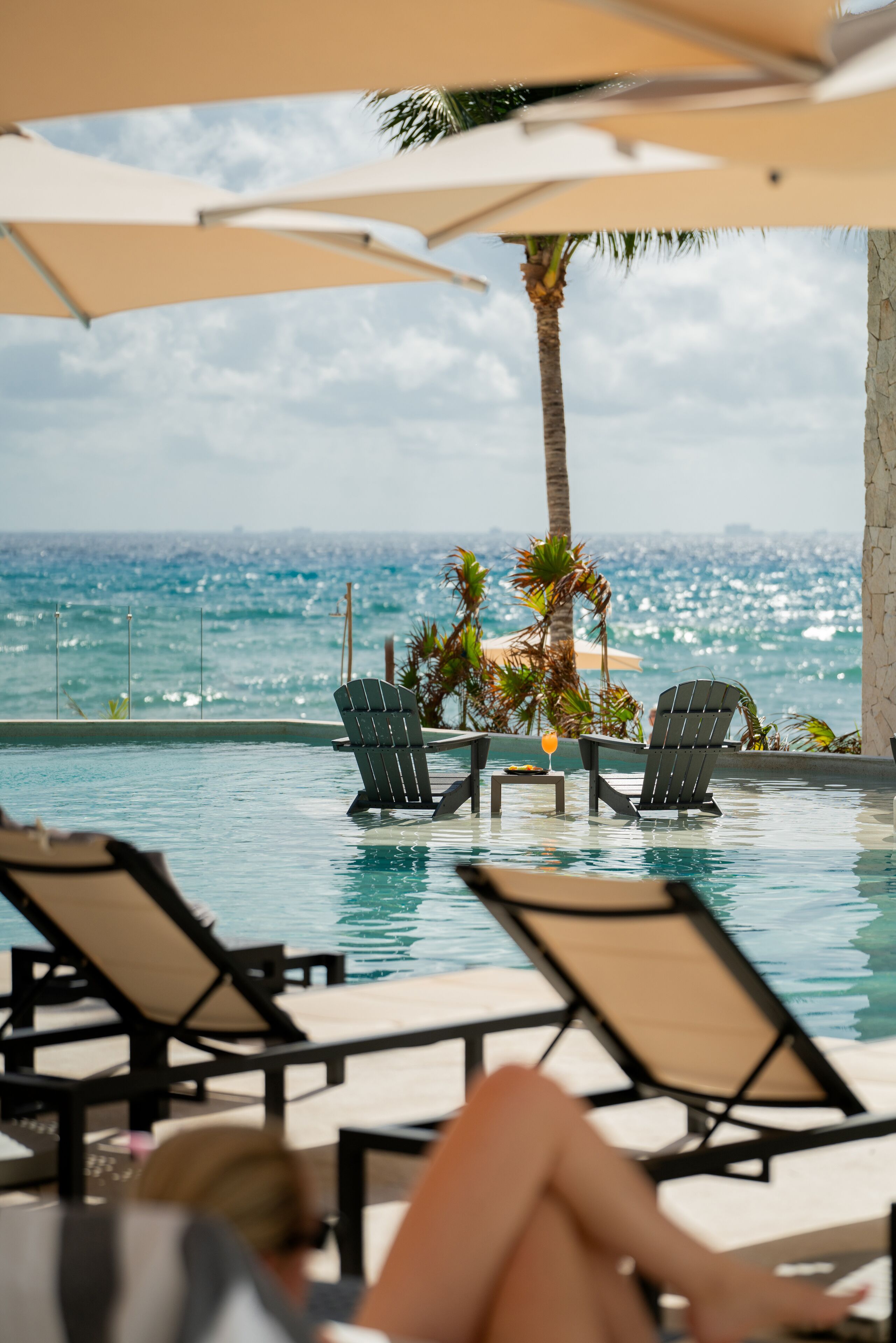 A poolside area with lounge chairs and umbrellas, overlooking a body of water with a view of the ocean.
