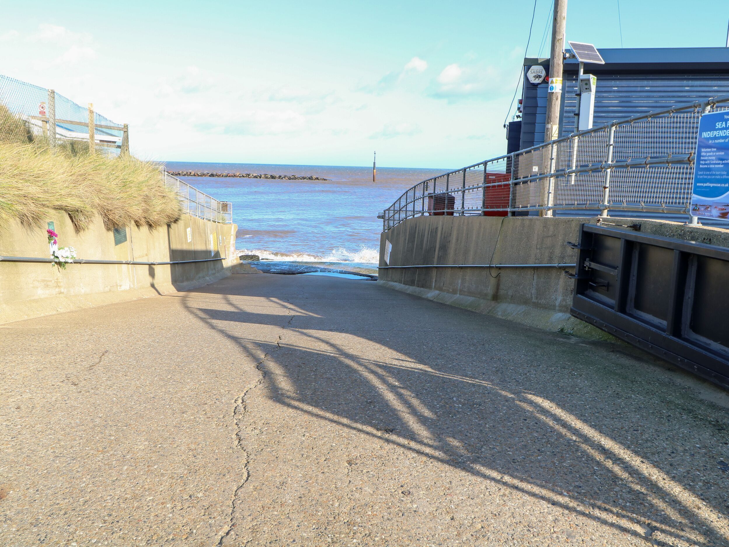 A coastal road leading to the sea with a concrete barrier on one side and a metal railing on the other.
